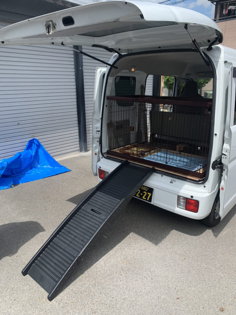 後部ドアを開け、折りたたみ式のスロープを地面まで下ろした軽バン。荷室にはペット用のケージを設置している